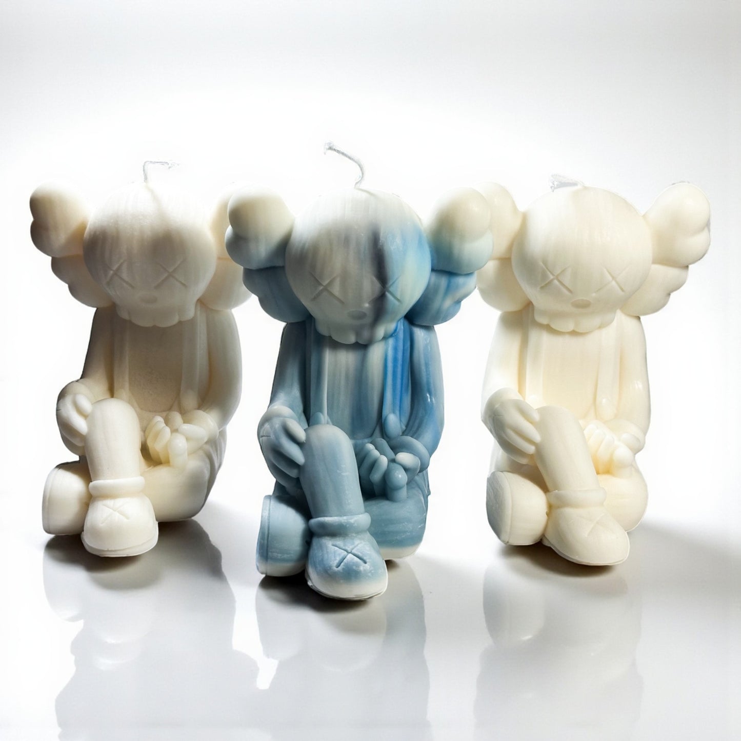 Three stylized bear figure candles in white, blue, and beige on a reflective surface with a white background.