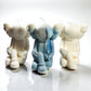 Three stylized bear figure candles in white, blue, and beige on a reflective surface with a white background.