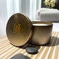 Travel tin Candle with a gold lid featuring Happy Scents logo on a wooden surface.
